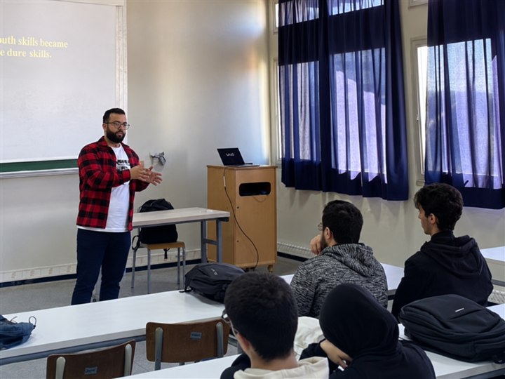 Abdellah explaining a topic beside a whiteboard while students listen in a classroom